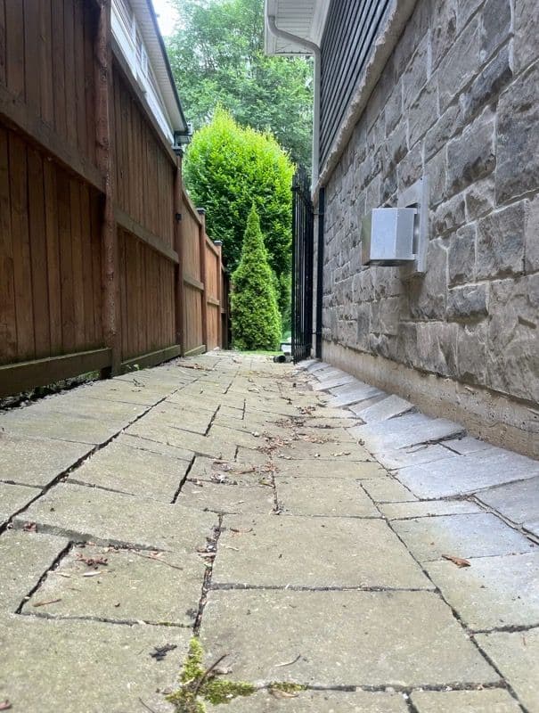 Narrow stone path between wooden fence and stone wall with greenery in background.