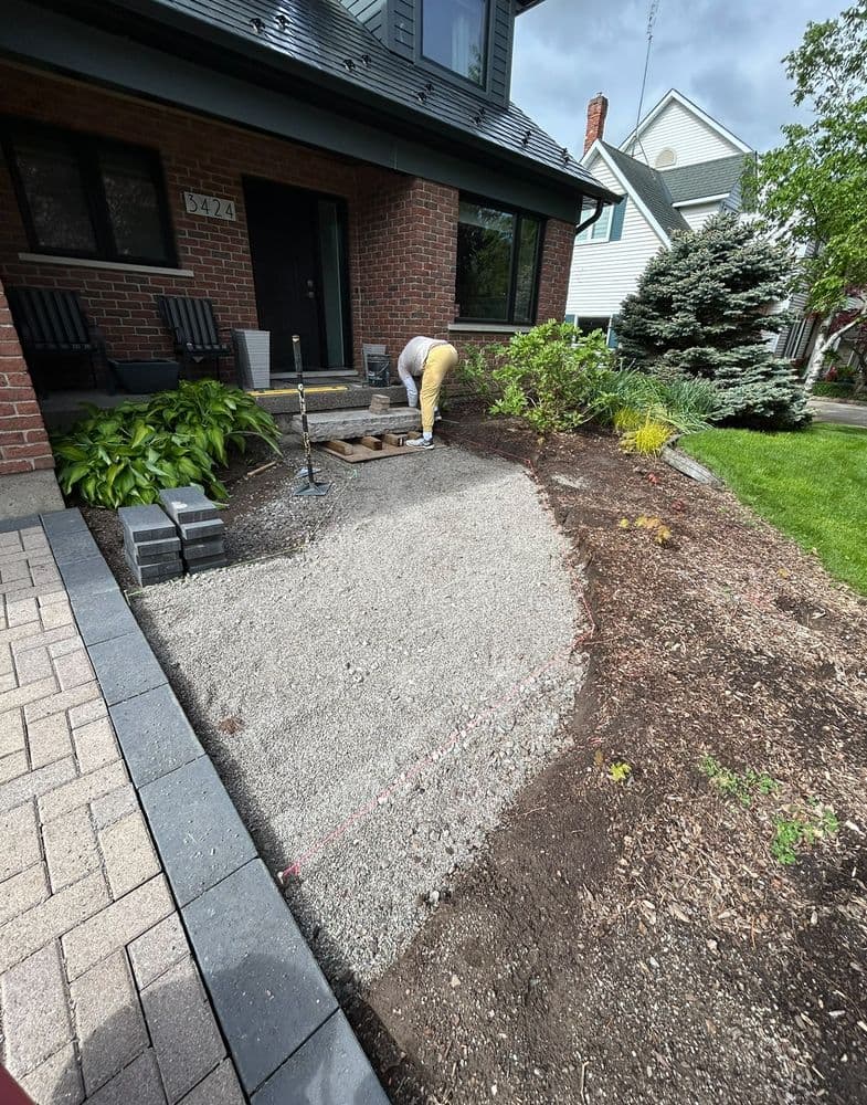 Person working on landscaping a front yard with gravel and garden beds.