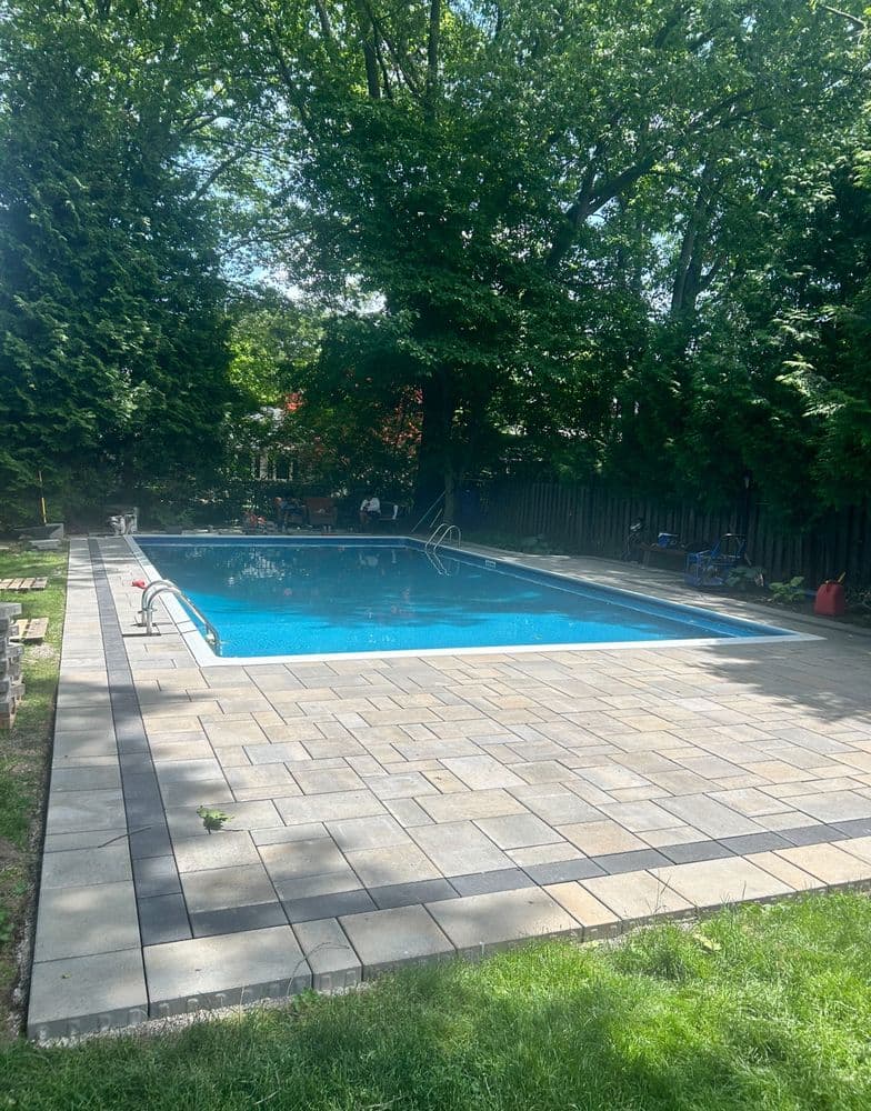 Rectangular outdoor swimming pool surrounded by greenery and paved patio area.