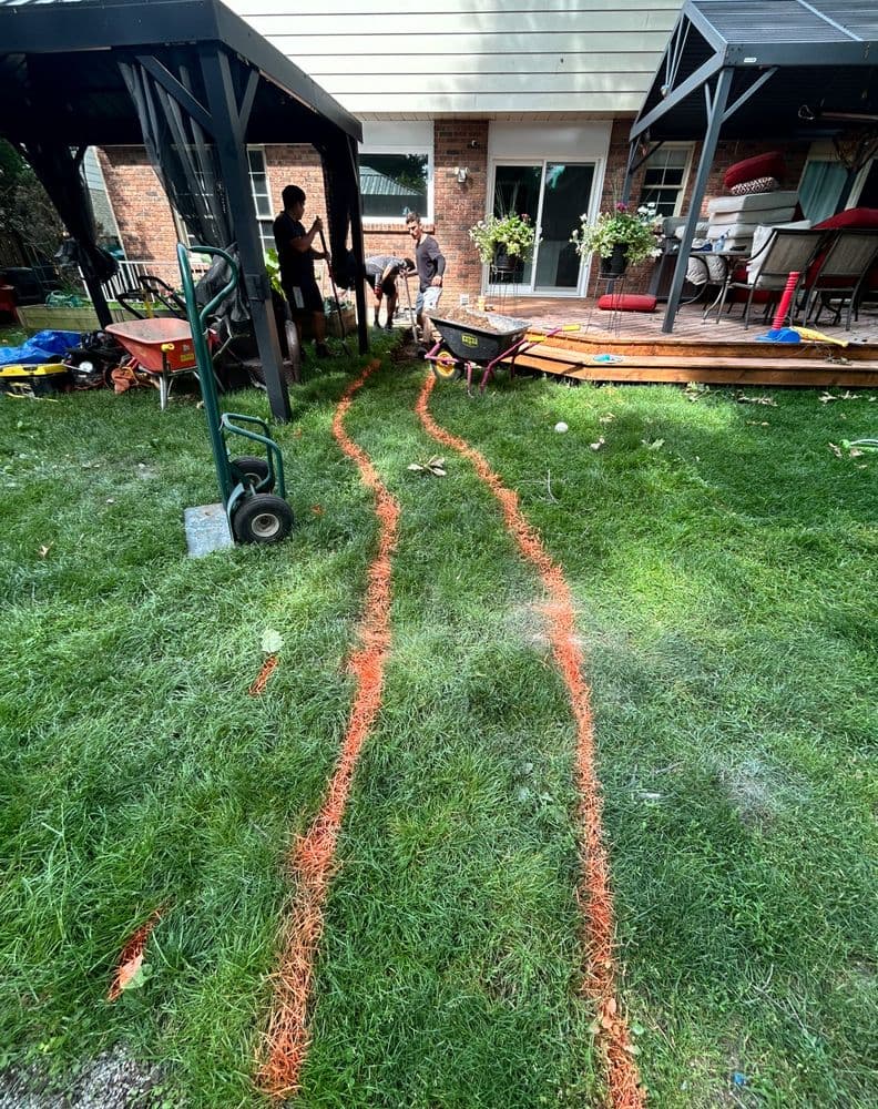 Lawn with orange marks showing landscaping work in progress near a patio and garden tools.