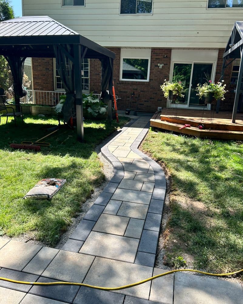 Curved stone pathway leading to a patio in a landscaped backyard with gazebos.